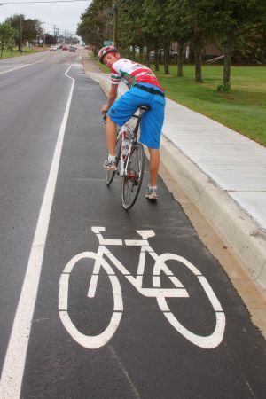 Young cyclist who is riding in a bike lane is looking over his shoulder to merge into traffic as the bike lane ends