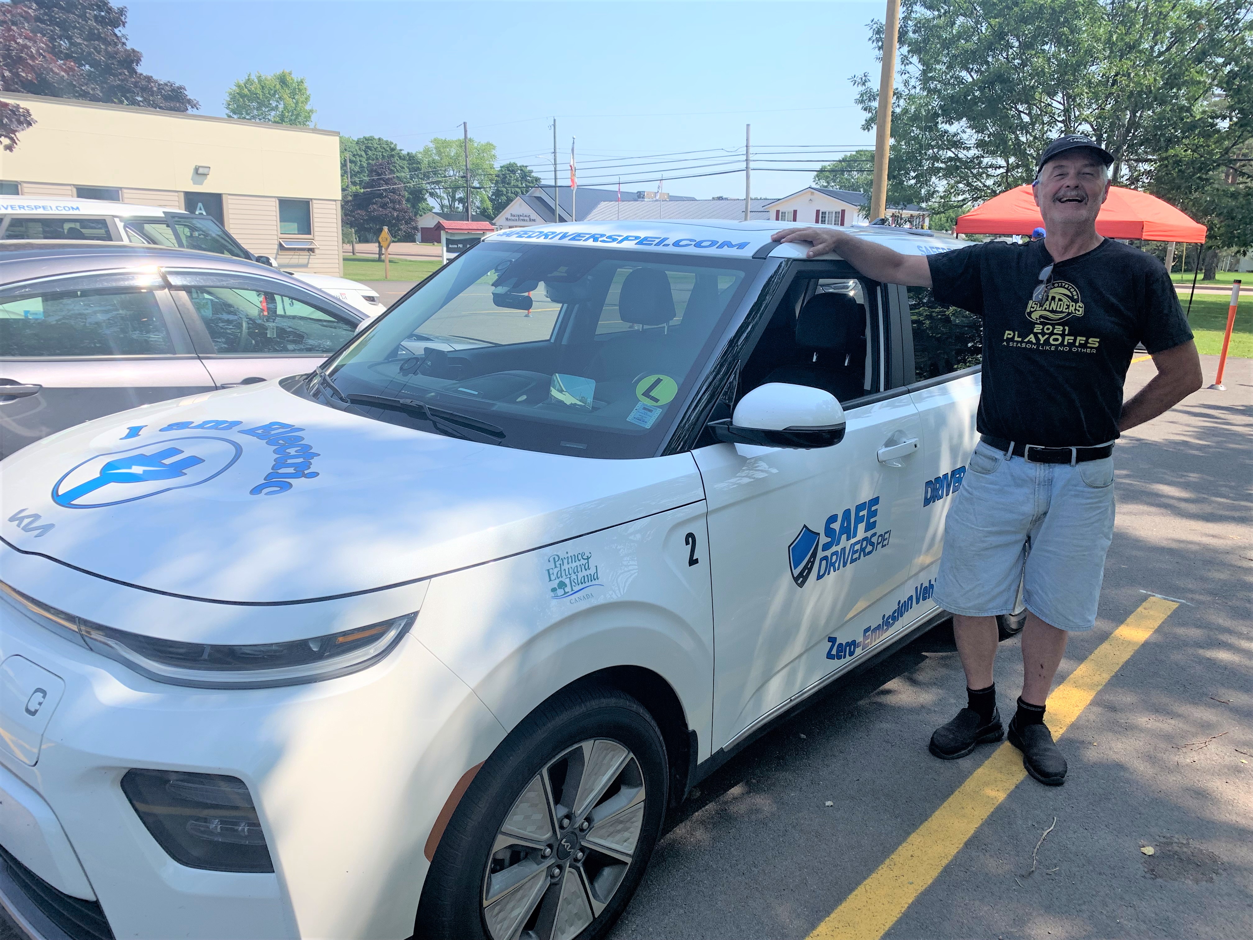 image of a person smiling and standing beside a white electric vehicle with his righthand on the roof.