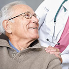 photo of man with grey hair sitting down and smiling health care provider standing behind him