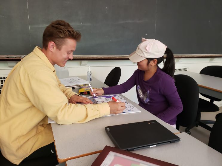 Tutor and young child sitting together at a table colouring