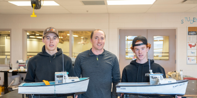 image of three people standing shoulder to shoulder hold a model fishing boat
