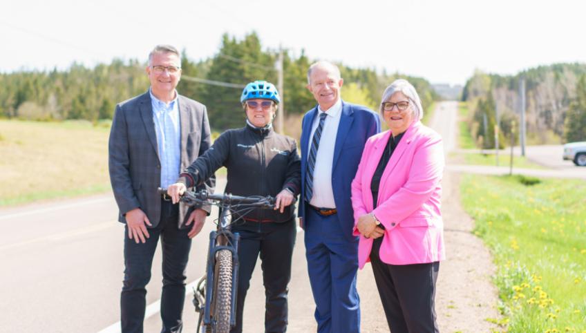 image of four peole standing shoulder to shoulder beside a road and one person holding onto a bicycle