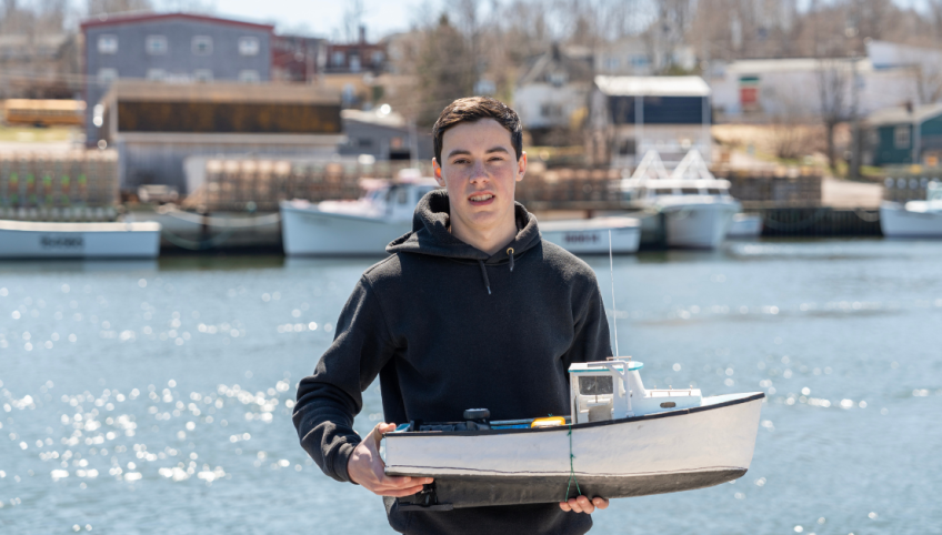 image of a person holding a model fishing boat at a wharf with fishing boats in the background