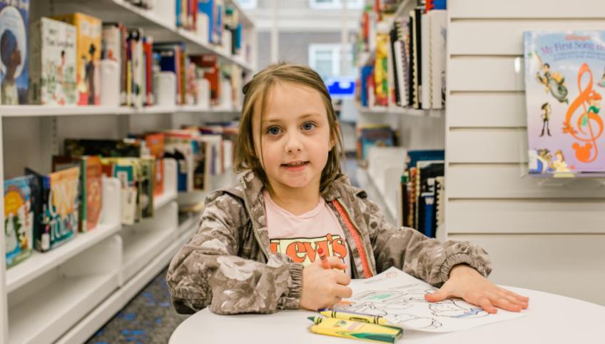 image of a child sitting at a table colouring with crayons in a libraray