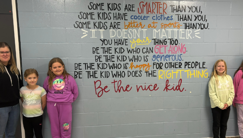 image of a teacher and elementary students standing near a wall with some inspirational writing on it.
