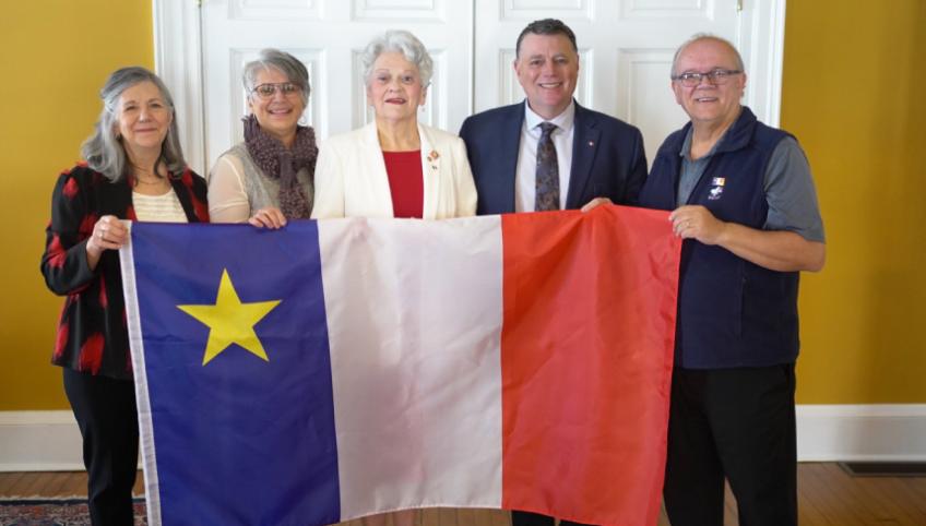 image of five people standing shoulder to shoulder holding a large Acadian flag in front of them