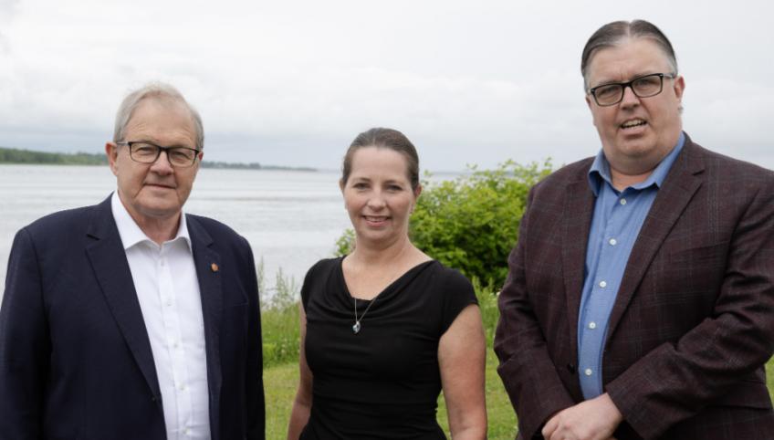 image of three people standing shoulder to shoulder with a bay of water in the background