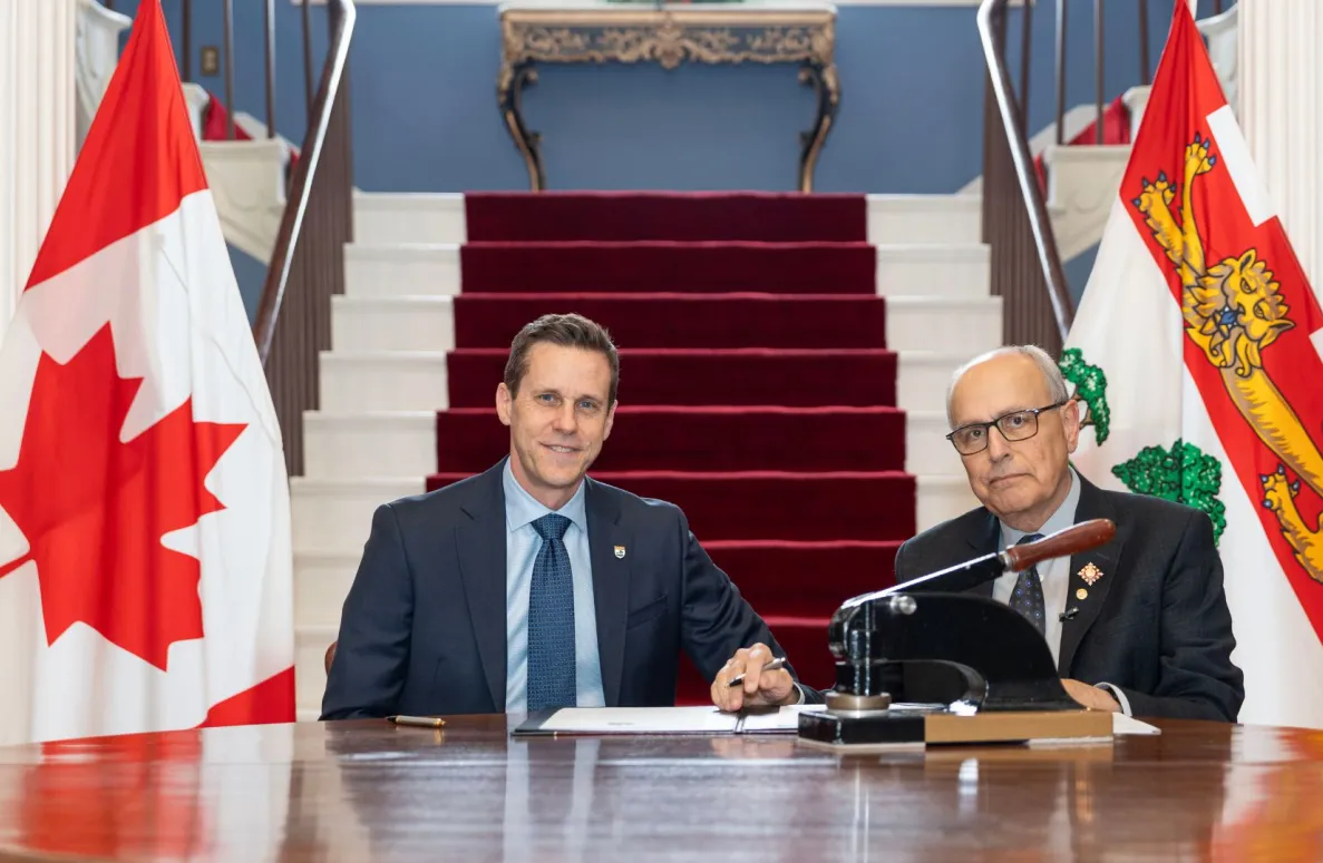 The premier and the lieutenant governor seated between two flags.