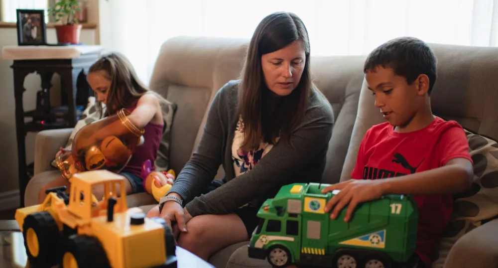 adult sitting on a couch playing with two children with toys