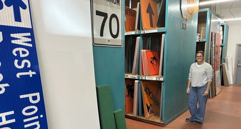 A woman stands beside shelves of transportation signs.