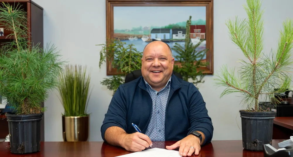 The Minister sits at his desk with different types of sapling trees around him.