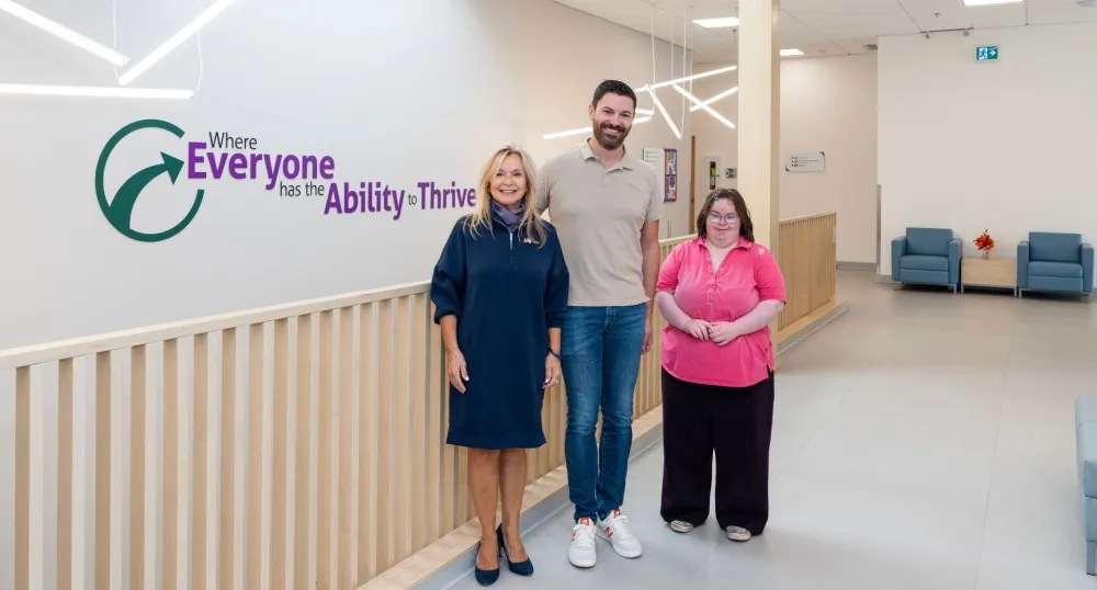 Three people stand in front of a wall with a motivational quote.