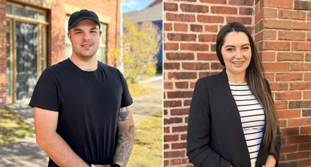 A photo of a man and a woman with brick a building behind them.