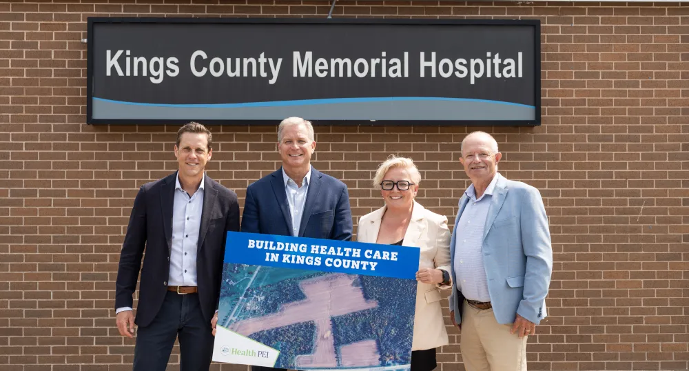 Trois hommes et une femme se tiennent devant le panneau de l'Hôpital commémoratif du comté de Kings tout en tenant une affiche du terrain nouvellement acquis.