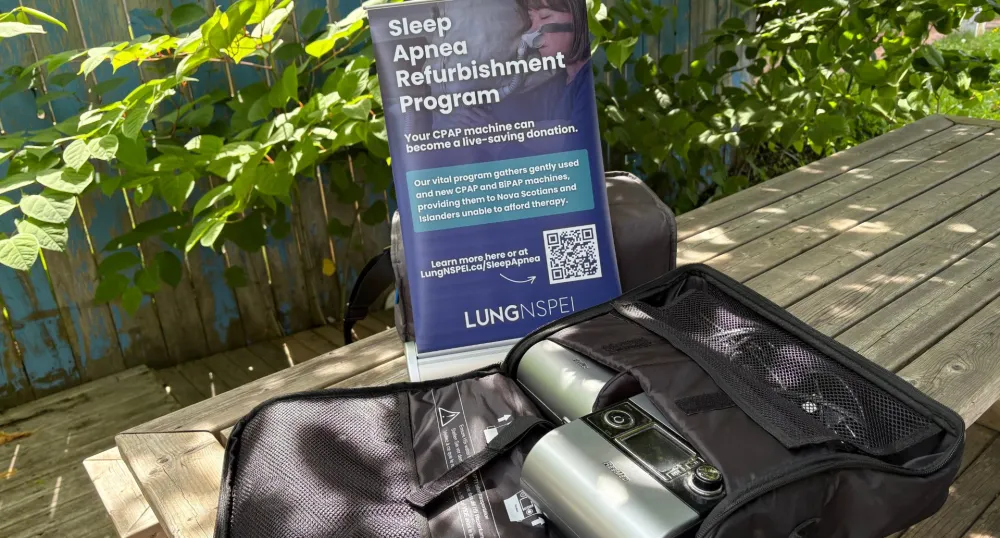 Une machine à apnée du sommeil est posée dehors sur une table de pique-nique entourée de feuillage vert.