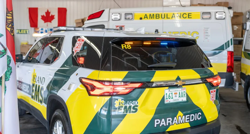 A yellow and green marked EMS van parked in front of an ambulance.