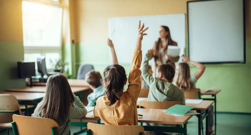 Students raising hands while teacher asking them questions in classroom