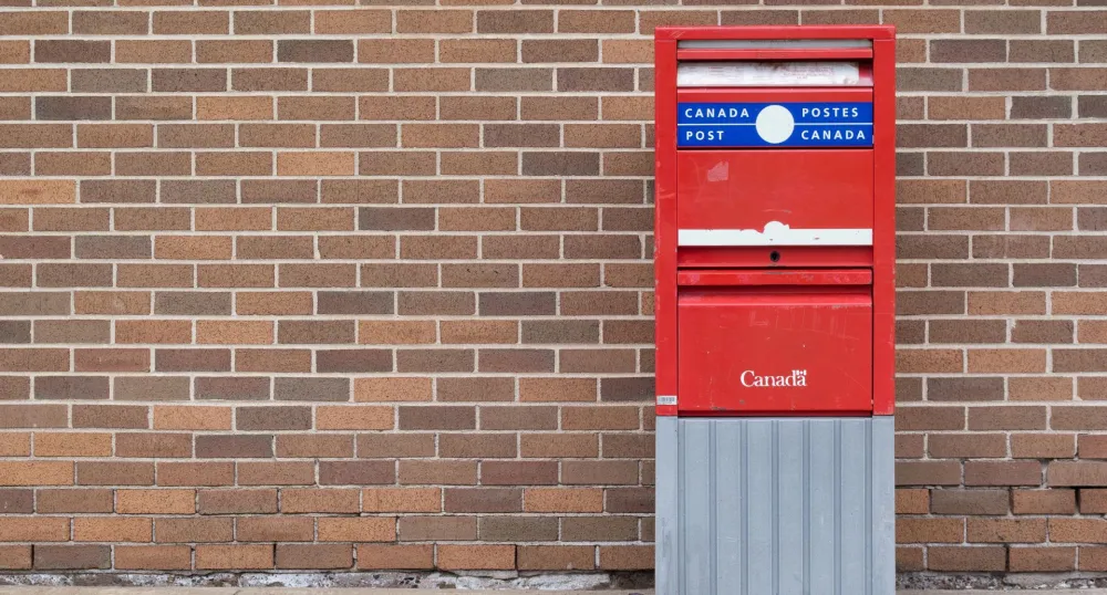 A red Canada post mailbox placed in front of a brick wall.