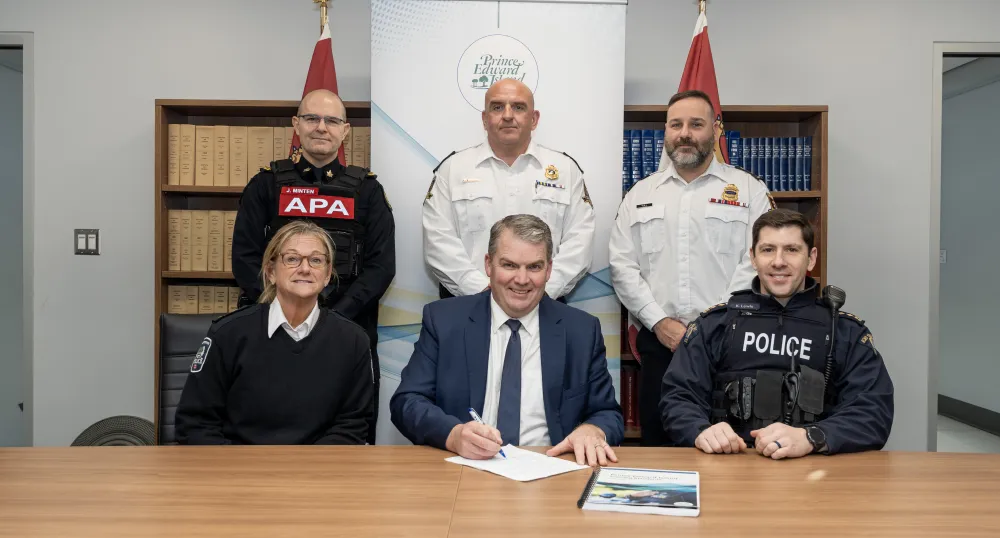 The minister and five officers stand in front of a bookcase.