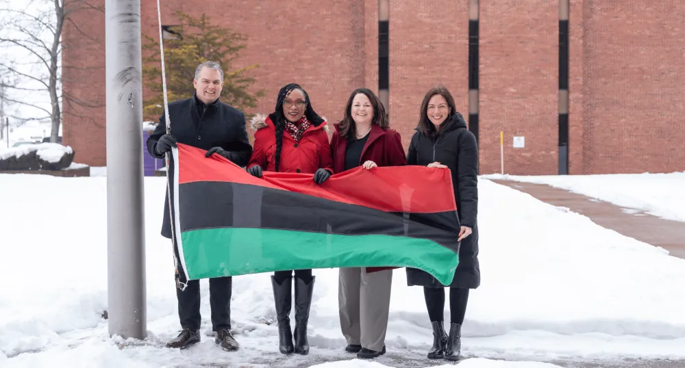 Quatre personnes se tiennent devant un drapeau à bandes rouge, noire et verte.