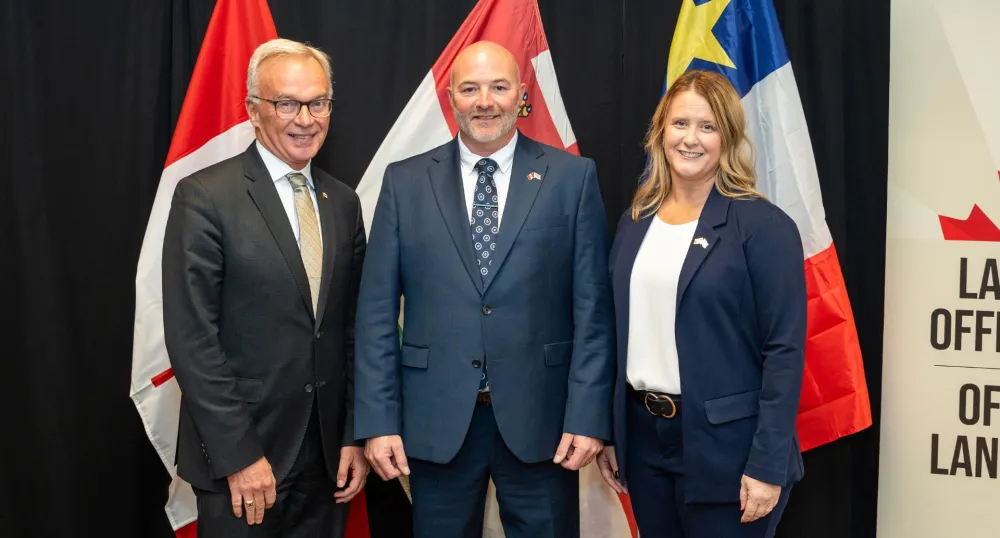 Trois personnes se tiennent devant des drapeaux.