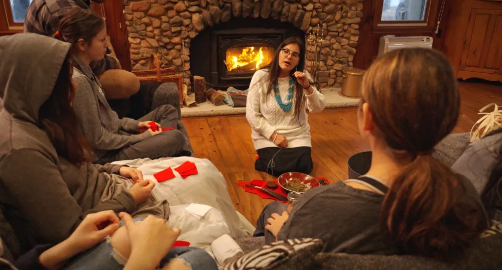 A cozy scene of people sitting around a woodstove.