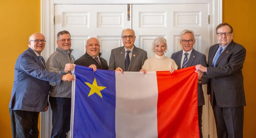 Seven adults hold a large Acadian flag.
