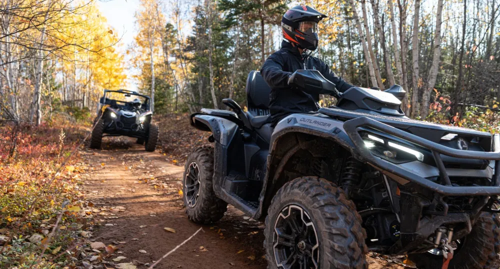 Two ATVs drive down a red dirt road in Autumn.