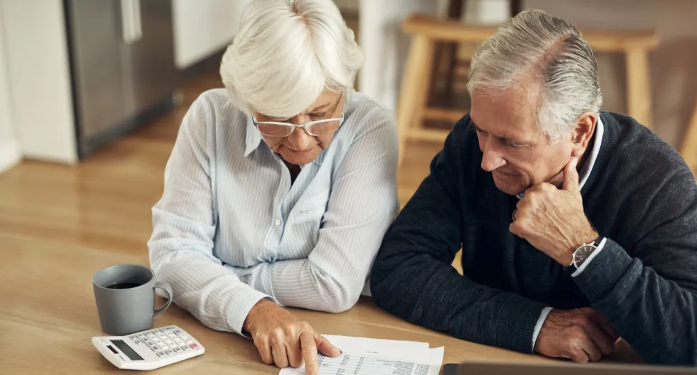 An elderly couple look over tax forms at their kitchen table.