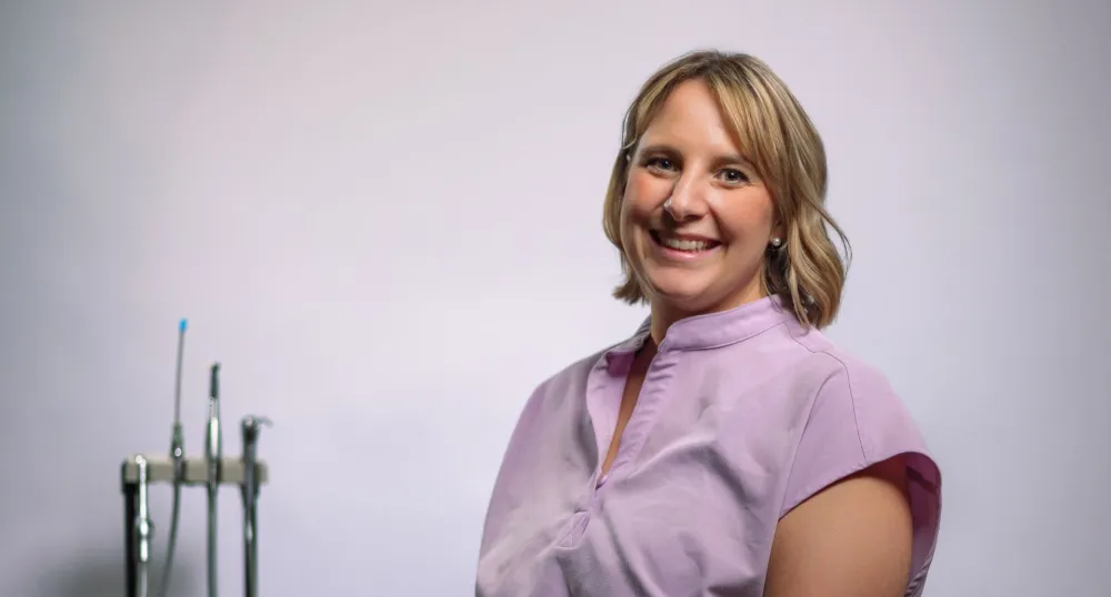 Une femme aux cheveux blonds mi-longs portant une tenue médicale rose.