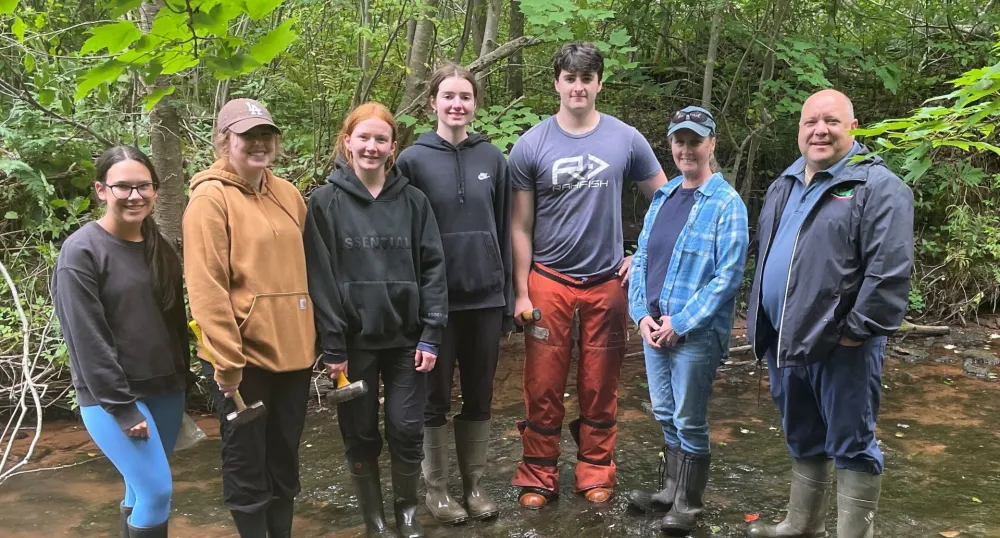 The Minister and watershed staff stand in the river with green foliage behind them.