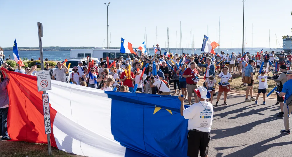 Many people celebrating in front of a large Acadian flag.
