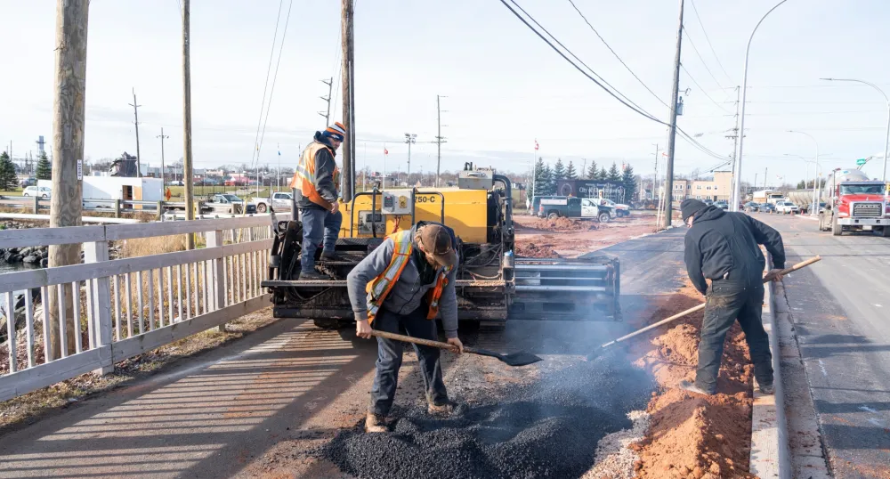 Three construction workers placing asphalt on an active transportation pathway in Prince Edward Island.