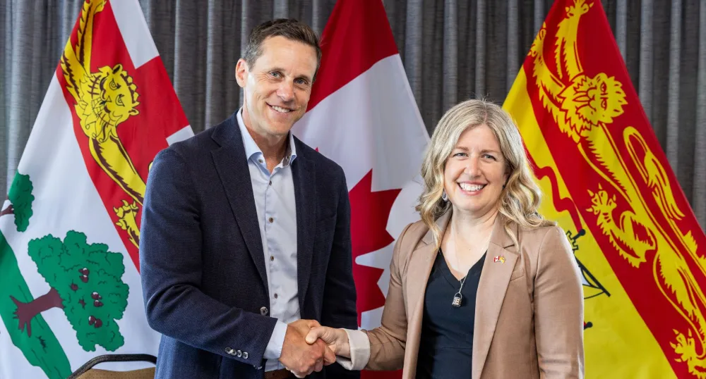 Les Premiers ministre se serrant la main devant les drapeaux de l'Île-du-Prince-Édouard, du Nouveau-Brunswick et du Canada.