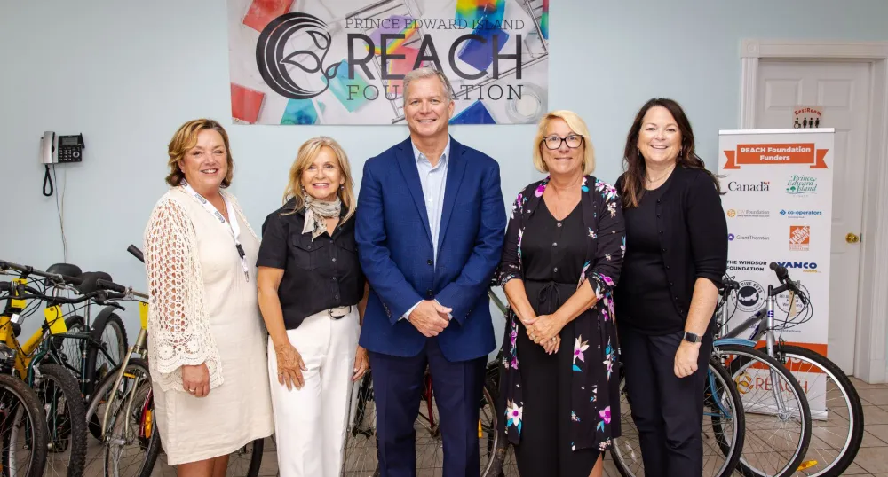 Cinq personnes se tiennent à côté de bicyclettes devant une affiche de la Reach Foundation.