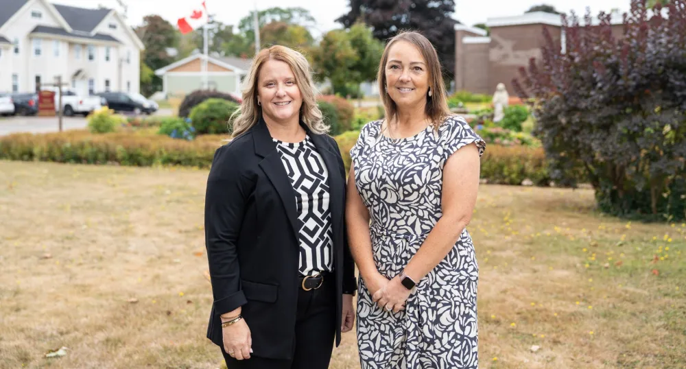 Two women stand next to each other outside.