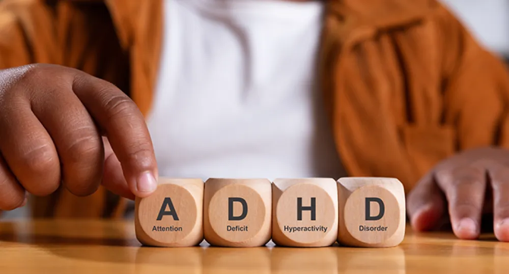 Hands of person spelling ADHD with wooden blocks on a table