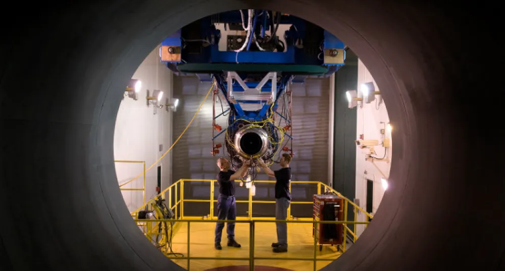 Two man standing and working in a workshop setting on an airplane part