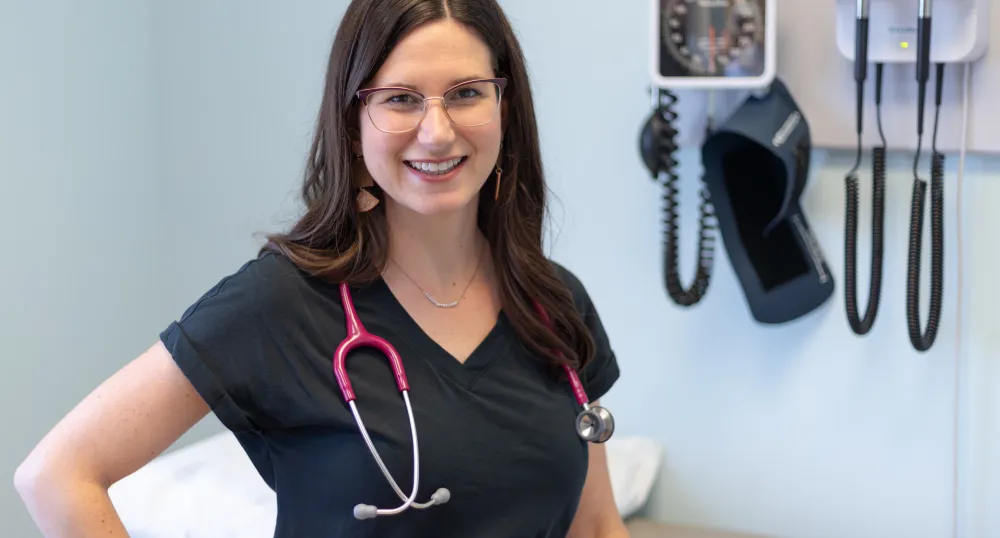 A smiling woman with a stethoscope around her neck in a clinic environment