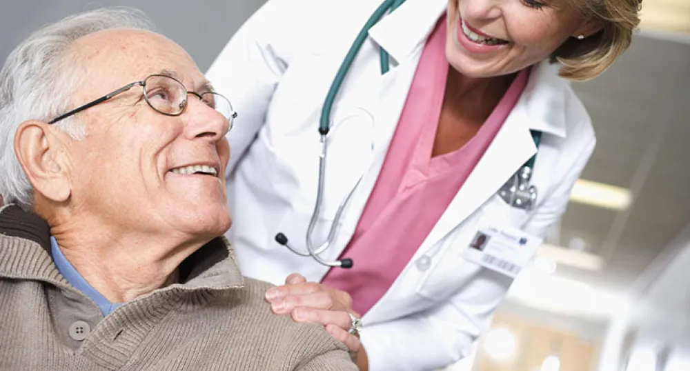 elderly man sitting down with smiling health care provider behind him