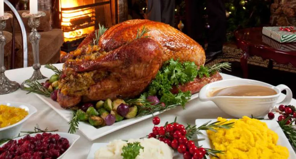 Image of dinner table set with roasted turkey, mashed potatoes, cranberry sauce and pickles