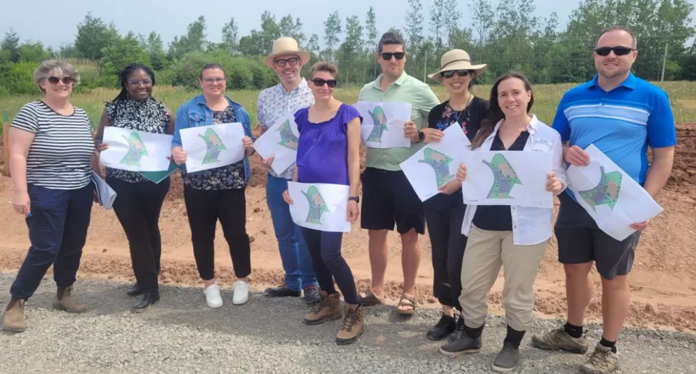 image of a small group of people standing shoulder to shoulder in an outdoor construction area while holding renderings of a building