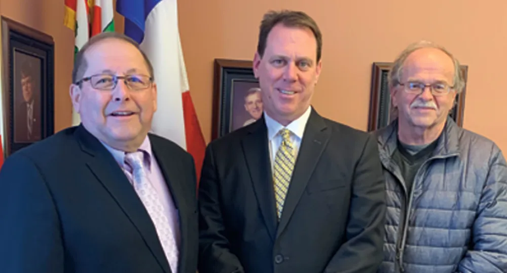 Three people stanindg shoulder to shoulder while in an office