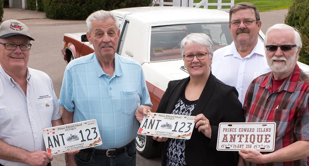 Five people holding an antiqye license plate.
