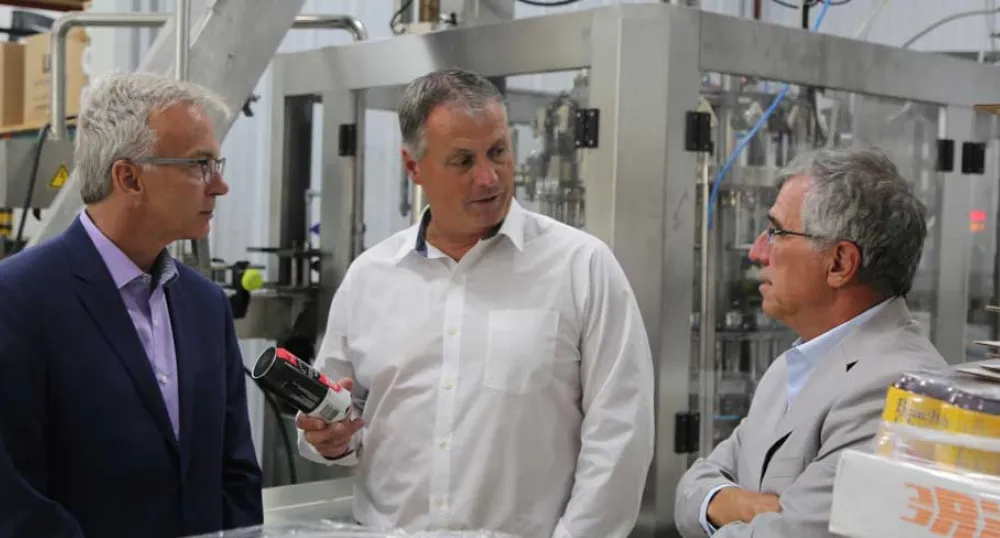 Photo shows three men standing amid brewing equipment