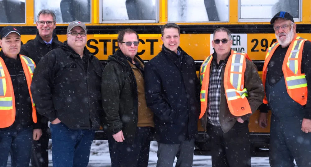 Minister Trivers and PSB Director Parker Grimmer stand outside beside a bus with school bus driver training participants