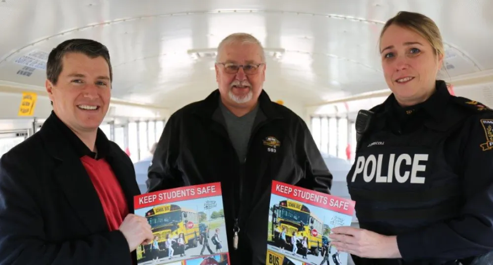 Three people stand inside a school bus holding school bus safety posters