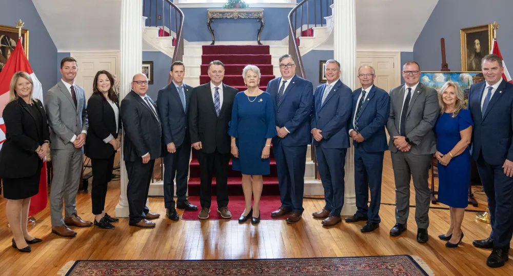 image of a group of people standing shoulder to shoulder inside a stately room in front of stairs