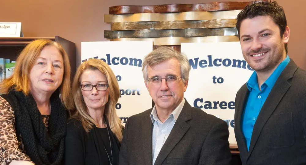 Minister Brown and three other people standing in front of Career Bridges sign and three of them are holding an information brochure.
