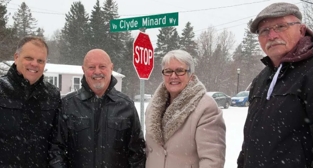 Minister Biggar and thre other people stand in front of the Clyde Minard Way street sign.